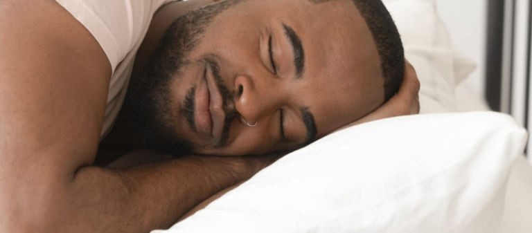 Smiling man sleeping soundly in bed – representing the importance of sleep for health, recovery, emotional balance, and wellbeing